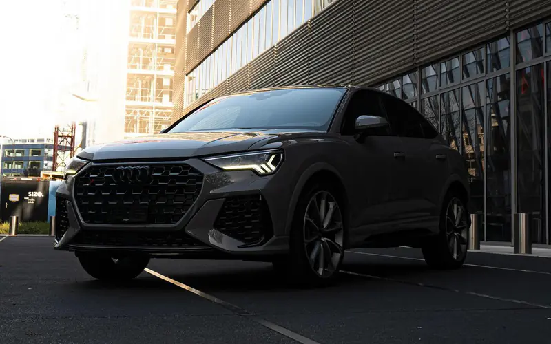 Audi RS Q3 grise vue de trois-quarts avant gauche, à l'arrêt devant un immeuble vitré dans la lumière du matin.