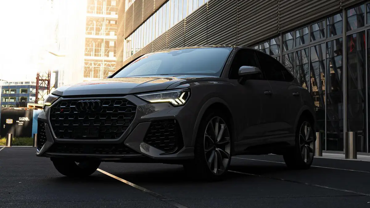 Audi RS Q3 grise vue de trois-quarts avant gauche, à l'arrêt devant un immeuble vitré dans la lumière du matin.
