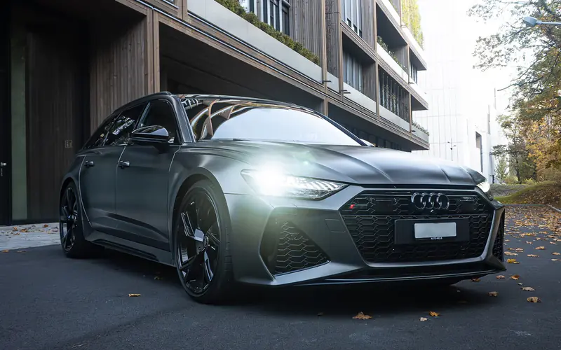 Audi RS6 grise mate vue de trois quarts avant, feux de jour allumés, devant un immeuble.