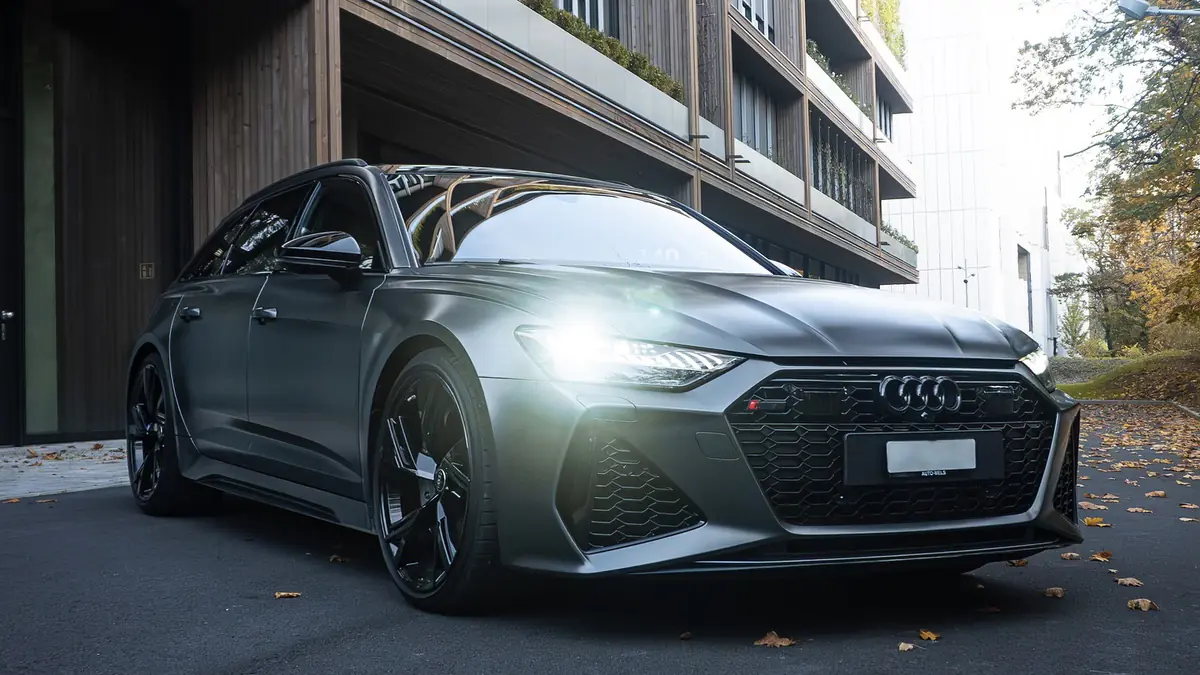 Audi RS6 grise mate vue de trois quarts avant, feux de jour allumés, devant un immeuble.