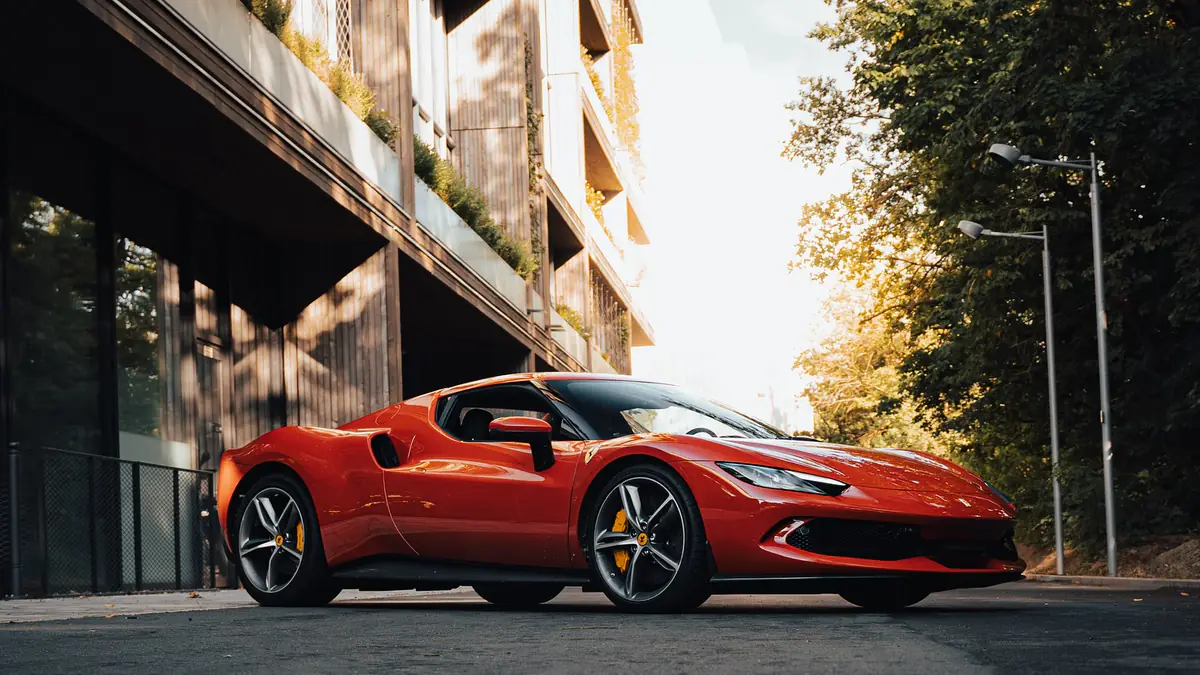 Ferrari 296 GTB Rosso Corsa vue de trois-quarts avant, voiture entière garée dans une rue baignée d'une lumière chaude.