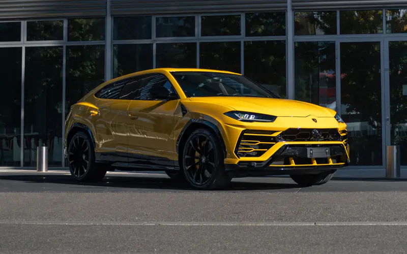 Lamborghini Urus jaune vu de trois quarts avant, garé devant une façade vitrée en plein soleil.