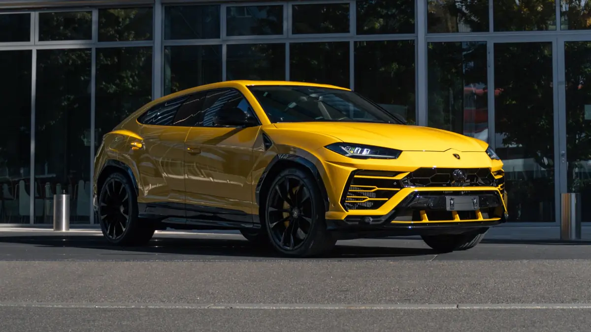 Lamborghini Urus jaune vu de trois quarts avant, garé devant une façade vitrée en plein soleil.