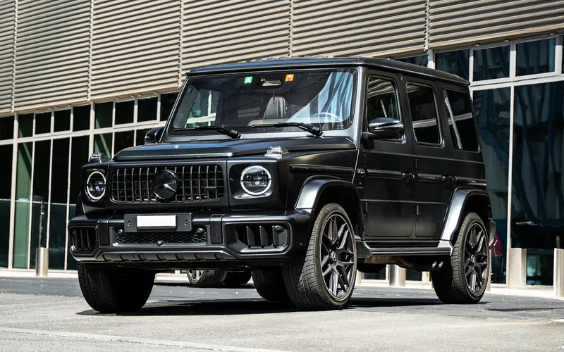 Mercedes-AMG G63 noir vu de trois quarts avant devant une façade vitrée.