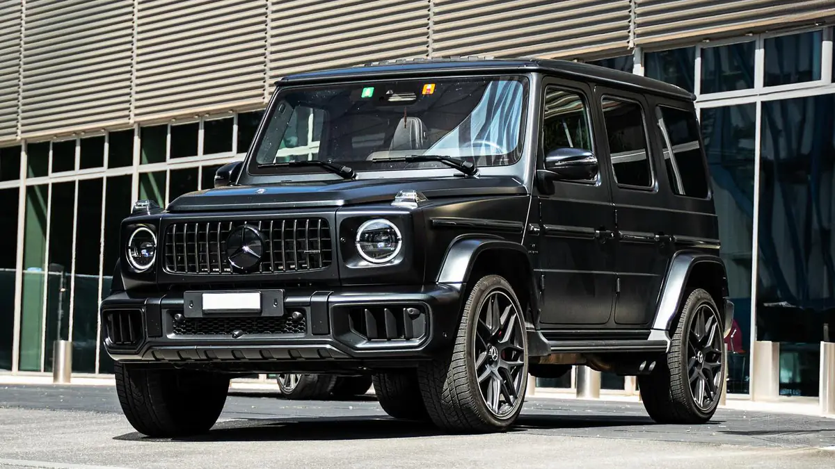 Mercedes-AMG G63 noir vu de trois quarts avant devant une façade vitrée.