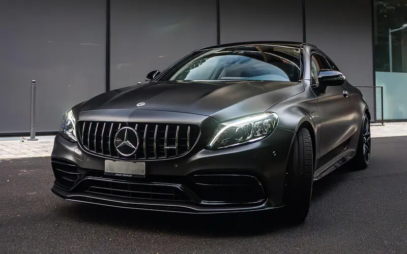 Mercedes-AMG C 63 coupé noir mat, vue de trois-quarts avant côté conducteur devant un immeuble moderne.