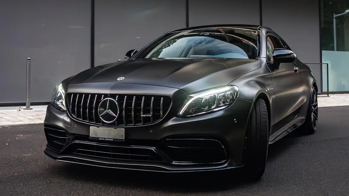 Mercedes-AMG C 63 coupé noir mat, vue de trois-quarts avant côté conducteur devant un immeuble moderne.