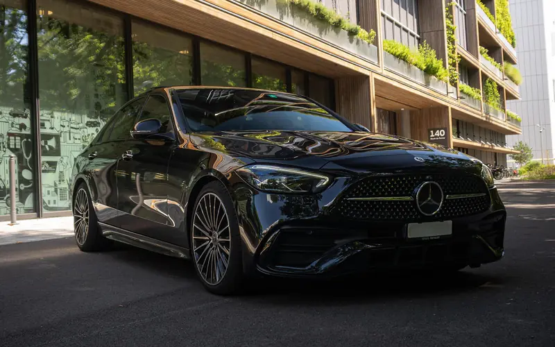 Mercedes Classe C 300 noire vue de trois quarts avant gauche, à l'arrêt devant un immeuble à façade végétalisée.