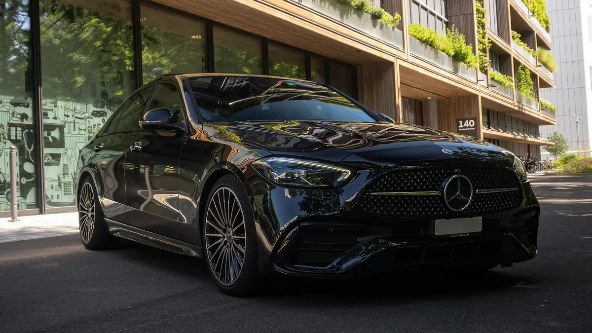 Mercedes Classe C 300 noire vue de trois quarts avant gauche, à l'arrêt devant un immeuble à façade végétalisée.