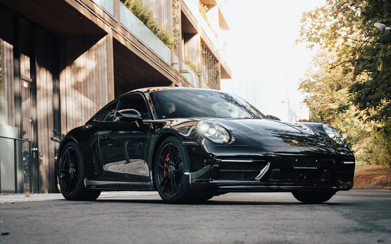 Porsche 911 Carrera GTS noire vue de trois quarts avant, garée dans une rue baignée d'une lumière dorée.