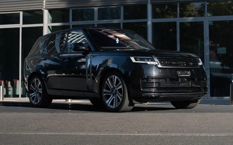 Range Rover Autobiography noir vu de trois quarts avant, garé devant une façade vitrée en plein soleil.