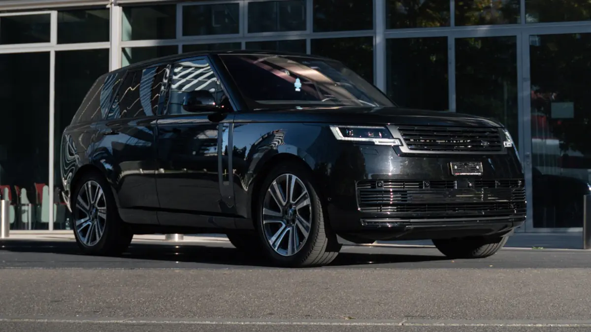 Range Rover Autobiography noir vu de trois quarts avant, garé devant une façade vitrée en plein soleil.