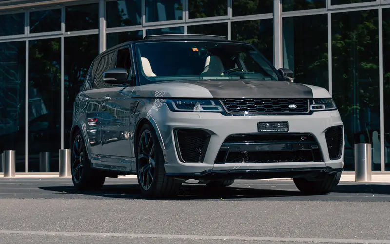 Range Rover Sport SVR gris Nardo Grey vu de trois quarts avant, à l'arrêt devant une façade vitrée.