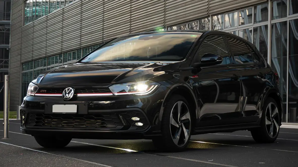 Volkswagen Polo GTI noire vue de trois quarts avant, phares allumés, devant un bâtiment moderne.